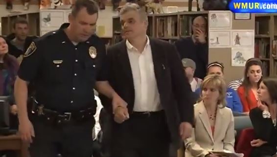 William Baer is lead out of a school board meeting by an armed officer who cuffs him in the hallway
